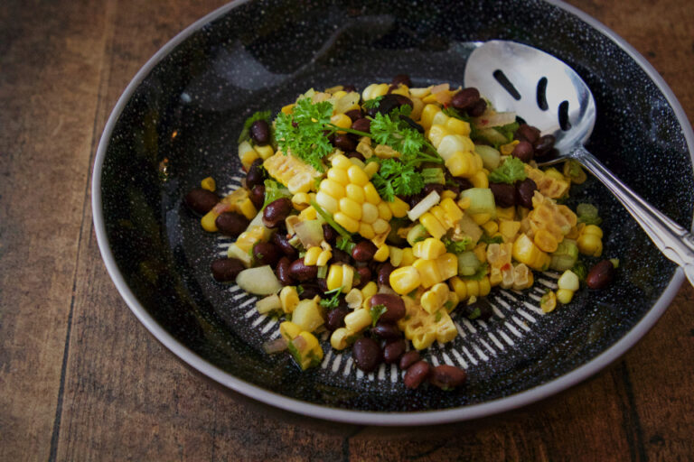 Dark bowl of corn, black bean and parsley salad on a wooden table, an example of a simple balanced plant-rich meal
