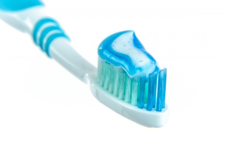 Blue toothbrush with a dab of blue toothpaste on its bristles against a white background, ready for daily brushing