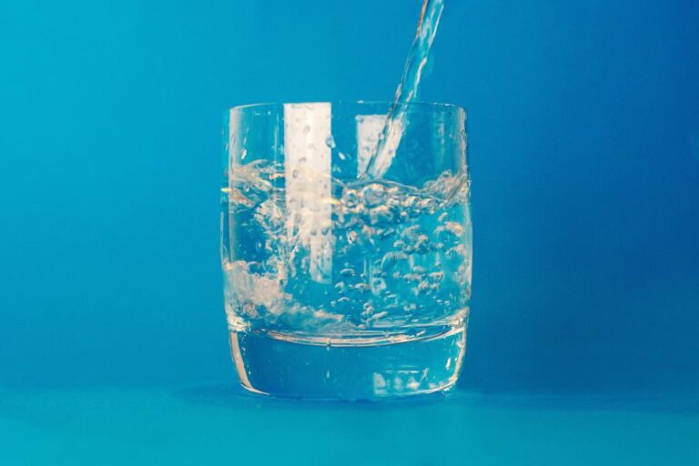 Water pouring into a clear glass against a blue background, a reminder to stay hydrated for bladder health