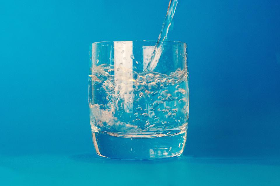 Water pouring into a clear glass against a blue background, a reminder to stay hydrated for bladder health
