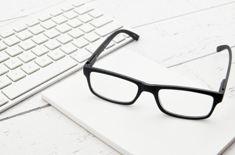 Black-framed eyeglasses resting on a white computer keyboard on a desk, a reminder to rest your eyes from screens