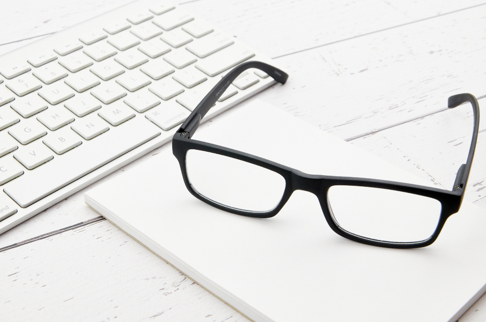Black-framed eyeglasses resting on a white computer keyboard on a desk, a reminder to rest your eyes from screens