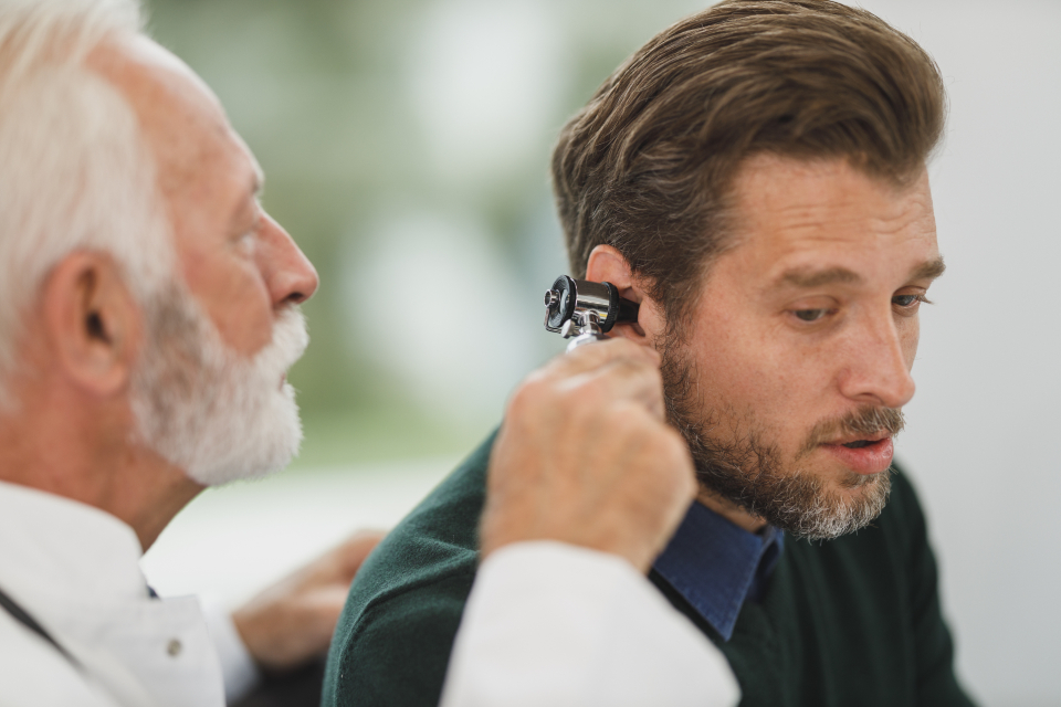 Doctor examining a man's ear with an otoscope during an ear check-up
