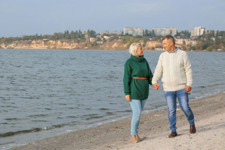 Older couple walking hand in hand along a shoreline path, a low-impact activity that suits many people with arthritis