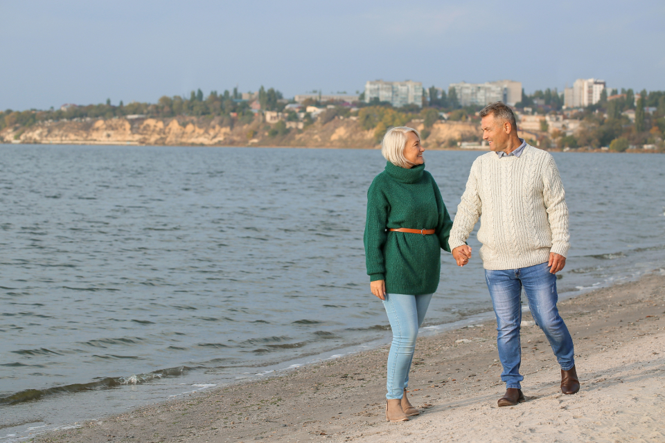 Older couple walking hand in hand along a shoreline path, a low-impact activity that suits many people with arthritis