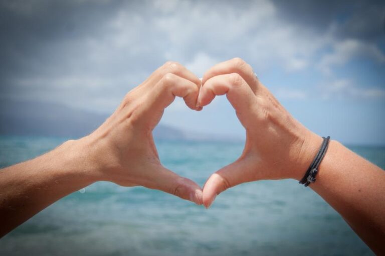 Two hands forming a heart shape against the sea and a cloudy sky, a symbol of caring for your heart health