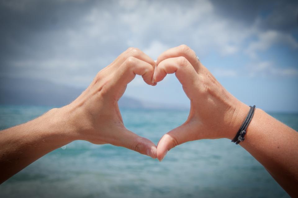Two hands forming a heart shape against the sea and a cloudy sky, a symbol of caring for your heart health