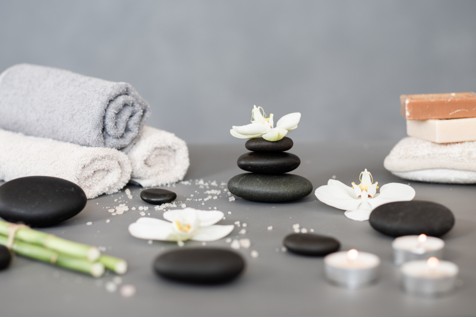 Stacked black stones, rolled towels, orchids and candles, a calming setup often used for soothing heat therapy