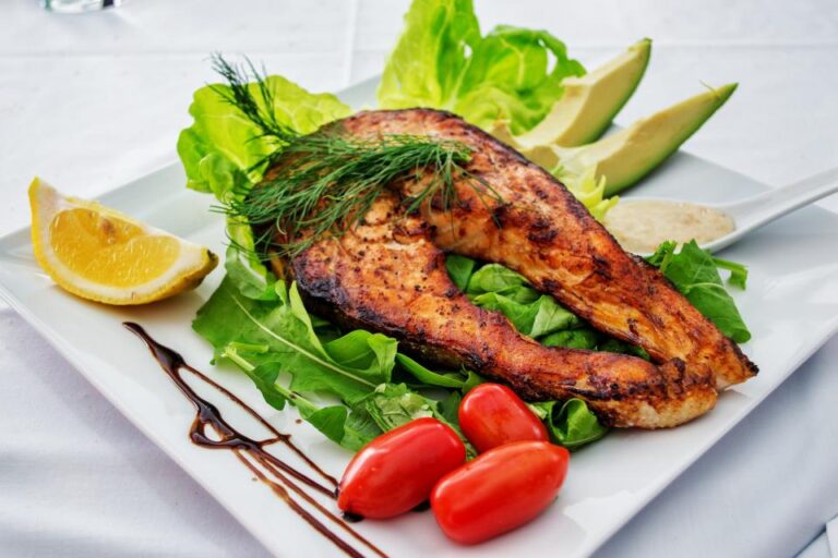 Grilled salmon with salad greens, avocado and cherry tomatoes on a white plate, an example of a balanced meal