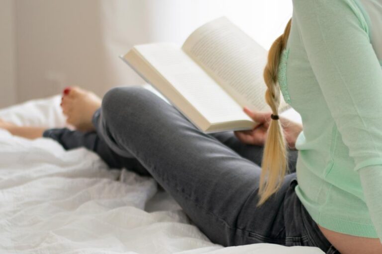 Woman reading a book on a white bed, a calming wind-down activity before sleep