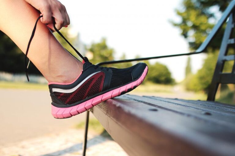 Woman lacing up a running shoe with her foot resting on a park bench, checking the fit before a walk or run