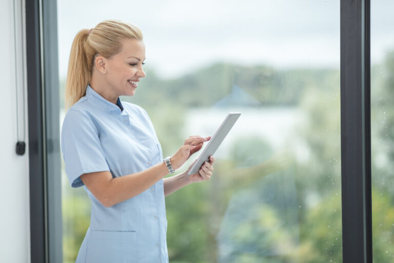 Smiling female healthcare professional checking a tablet beside a bright clinic window, ready for a women's health visit