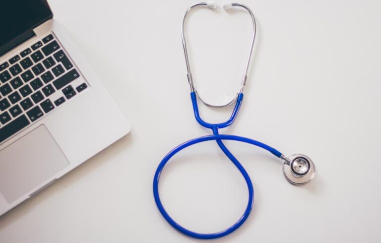 Stethoscope lying next to a laptop on a white desk, representing a telehealth visit with a doctor
