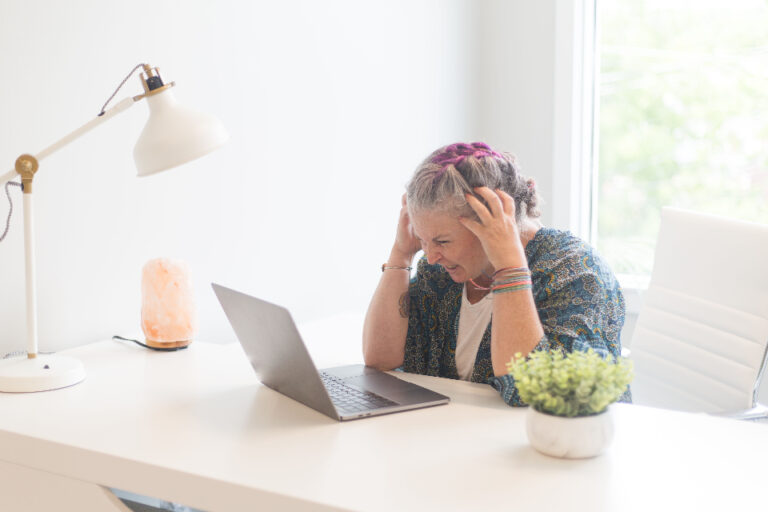 Woman at a desk holding her head in frustration while looking at a laptop, showing work-related stress