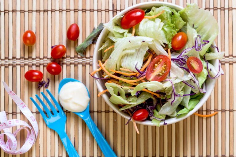 Bowl of fresh salad with cherry tomatoes beside a measuring tape, representing realistic weight goals