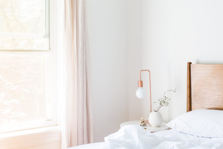Bright, calm bedroom with white bedding, a small lamp and a vase beside the bed, a restful setting for better sleep