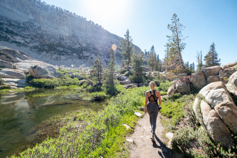 Woman walking along a sunny nature trail beside a pond, a gentle way to start a regular walking routine