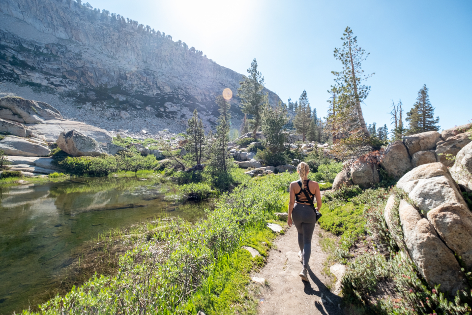 Woman walking along a sunny nature trail beside a pond, a gentle way to start a regular walking routine