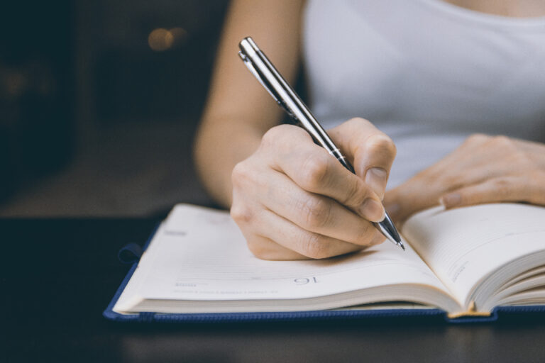 Woman writing in a notebook with a pen, keeping notes such as medicines and symptoms to share with her doctor