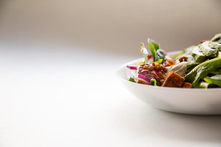 White bowl of fresh vegetable salad with lentils, spinach and red onion on a bright table