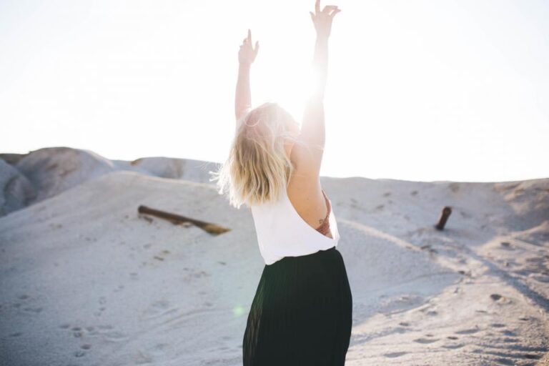 Woman with arms raised in bright sunlight on a sandy hill, a moment of relief and calm after letting go of stress