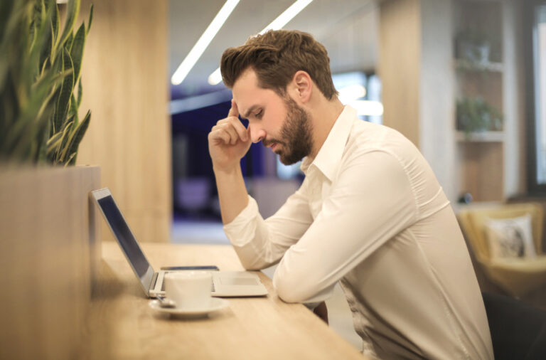 Man resting his head on his hand with a pensive look while sitting at a laptop, reflecting on how he feels