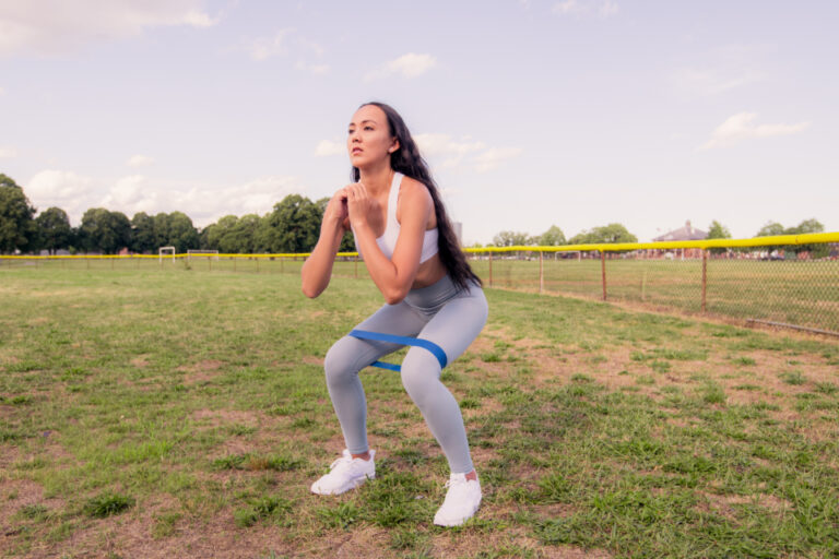 Woman doing a squat outdoors with a resistance band around her thighs to strengthen the muscles that support the knees