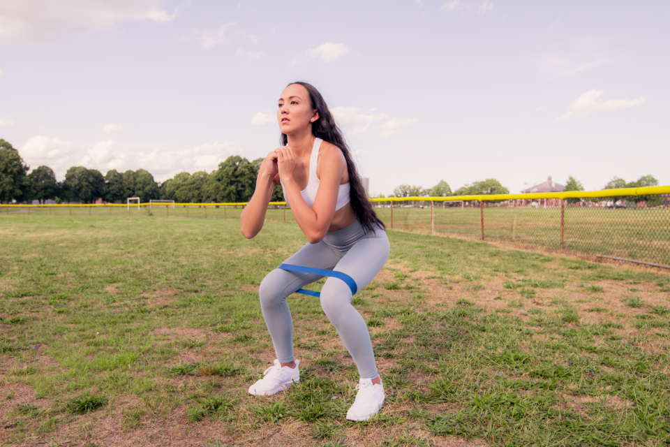 Woman doing a squat outdoors with a resistance band around her thighs to strengthen the muscles that support the knees
