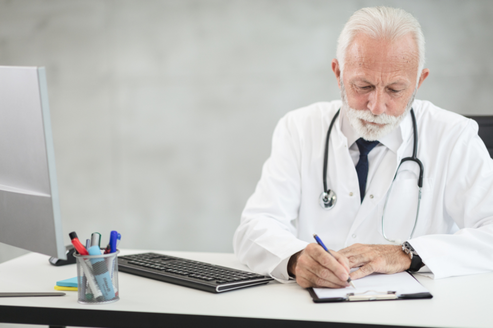 Doctor writing on a clipboard at a clinic desk, as when reviewing a patient's routine screening checklist