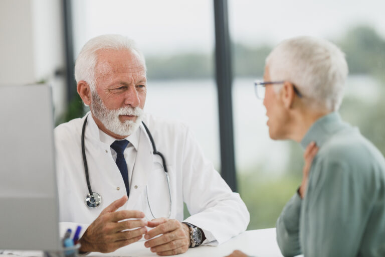 Doctor in a white coat listening to a woman patient during a consultation in a bright, modern clinic