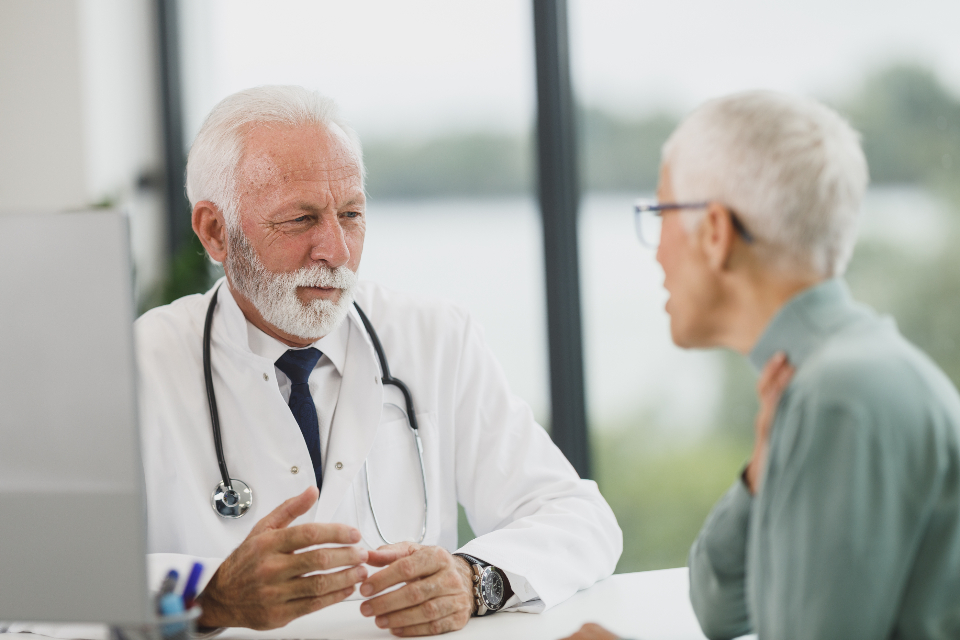 Doctor in a white coat listening to a woman patient during a consultation in a bright, modern clinic