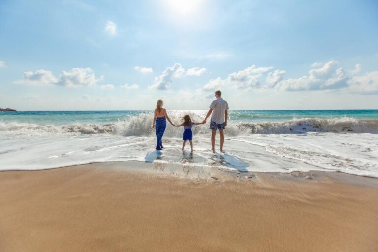 Parents holding hands with their young daughter at the edge of the sea on a sunny beach