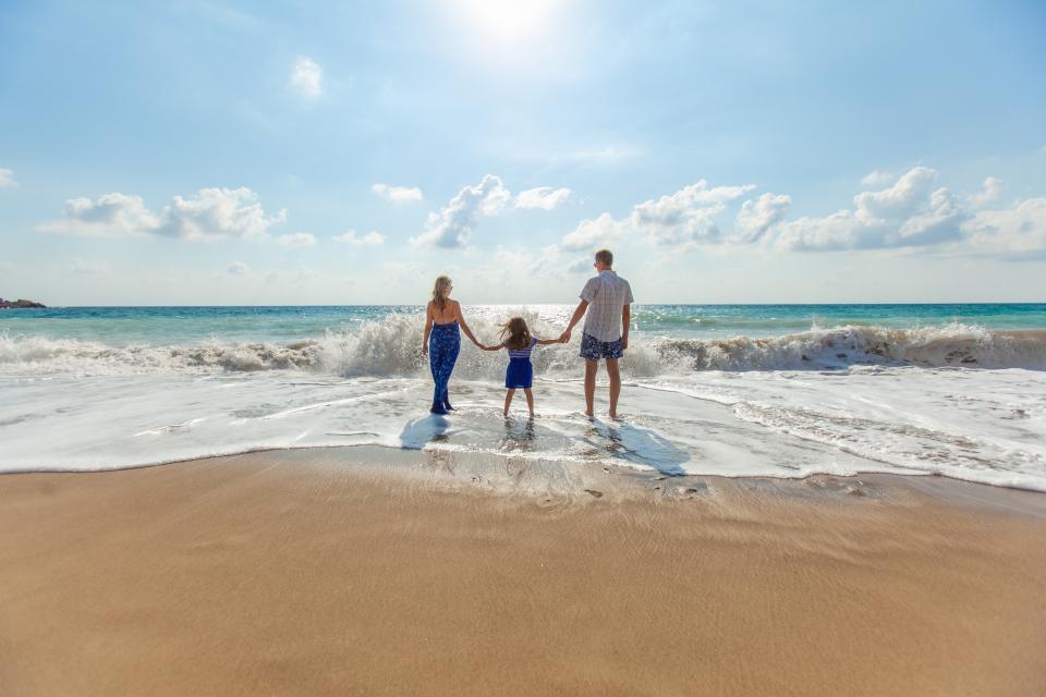 Parents holding hands with their young daughter at the edge of the sea on a sunny beach