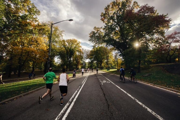 Two people jogging and cyclists riding on a tree-lined park road in autumn, an easy way to stay active outdoors
