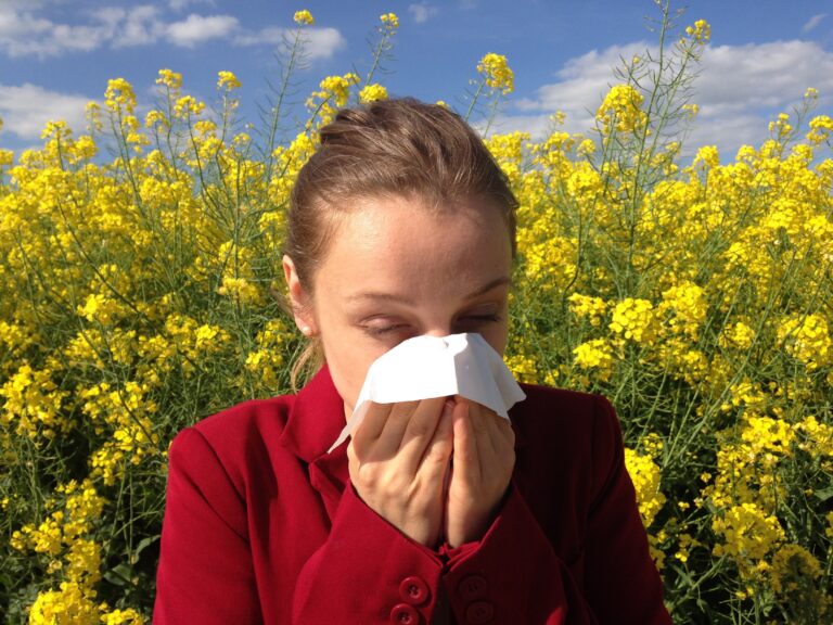 Woman blowing her nose into a tissue in front of a yellow flowering field, a typical seasonal pollen allergy scene