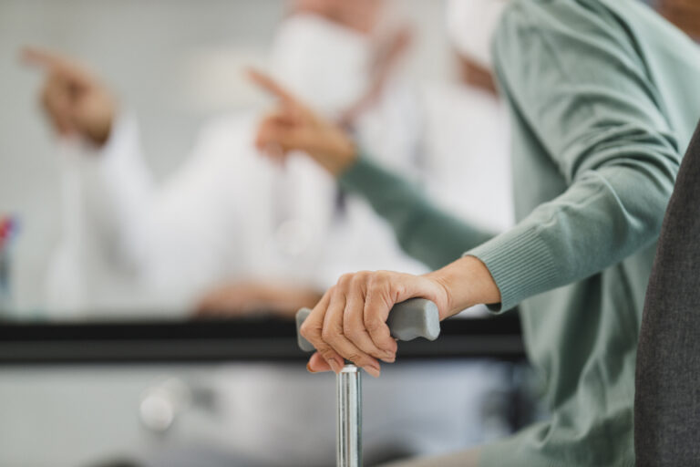 Older adult's hand resting on a walking cane in a clinic, a reminder to check balance and fall risk with a doctor
