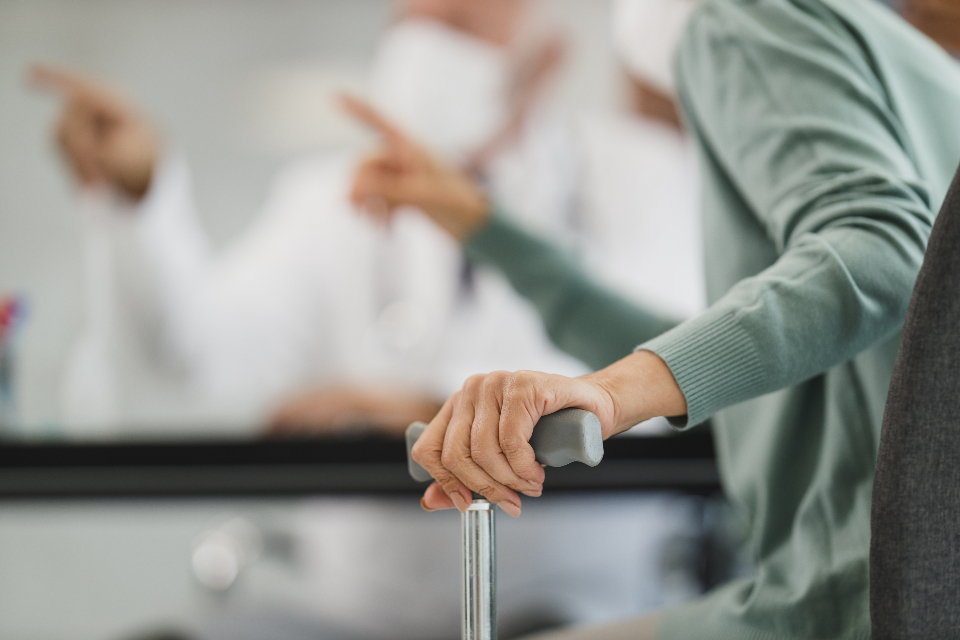 Older adult's hand resting on a walking cane in a clinic, a reminder to check balance and fall risk with a doctor