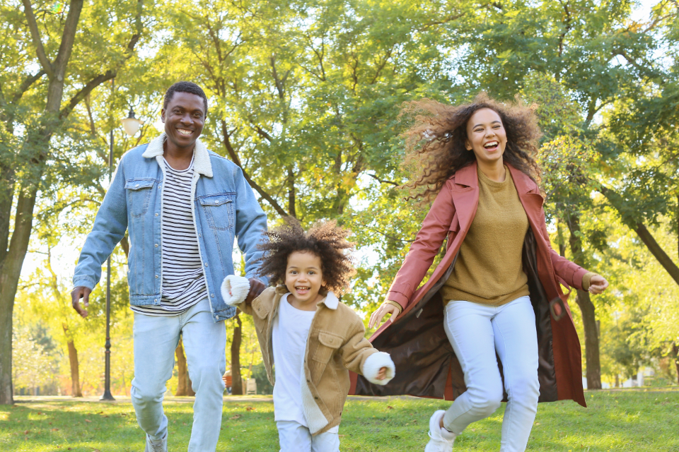 Parents and a young child running happily together through a sunny park
