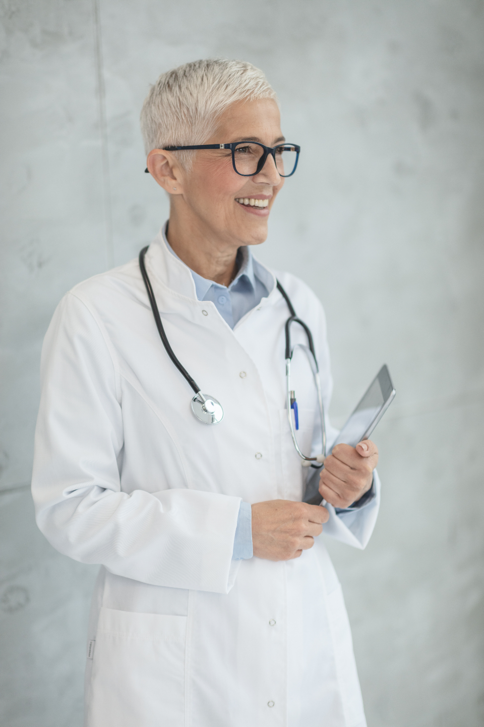 Smiling female doctor in a white coat with a stethoscope, holding a digital tablet