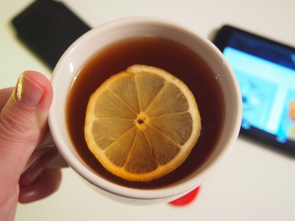 Hand holding a cup of warm tea with a slice of lemon, a soothing drink for a sore throat