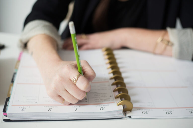 Woman writing in a daily planner with a pencil, tracking her menstrual cycle and symptoms