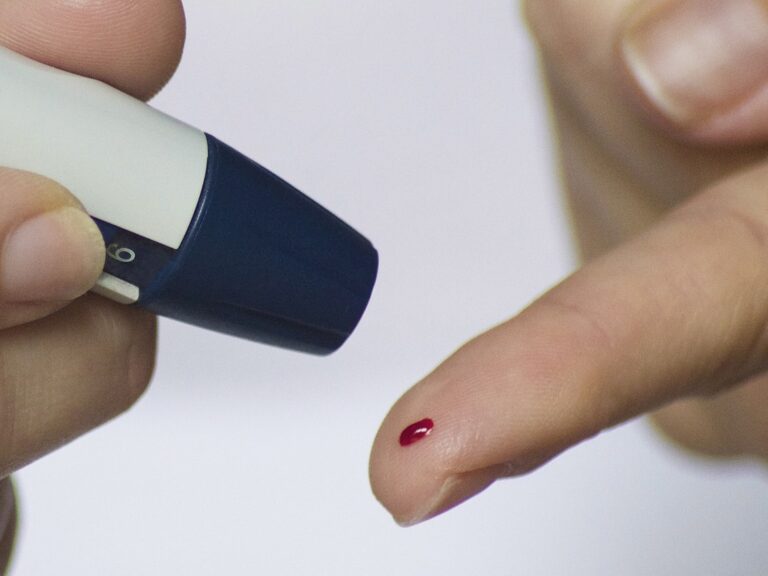 Fingertip with a drop of blood next to a lancing device, used to check blood sugar levels