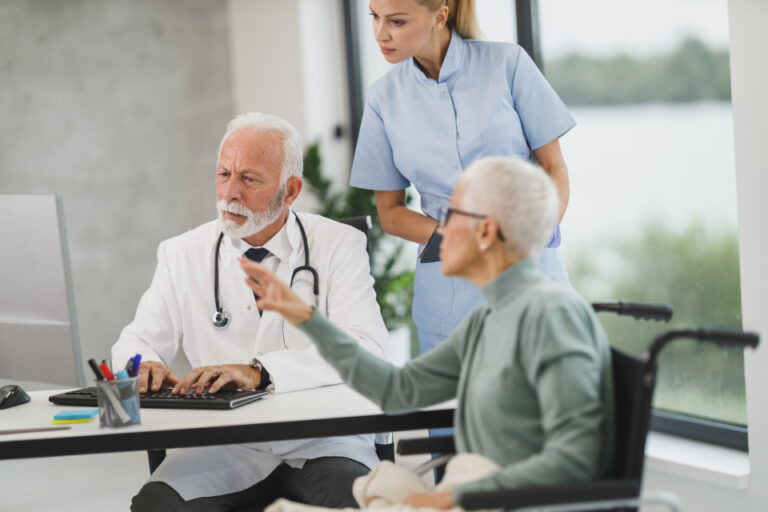 Doctor reviewing information on a computer with an older patient and a nurse during a consultation