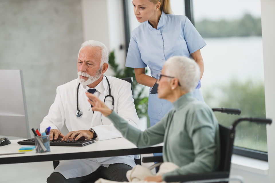 Doctor reviewing information on a computer with an older patient and a nurse during a consultation