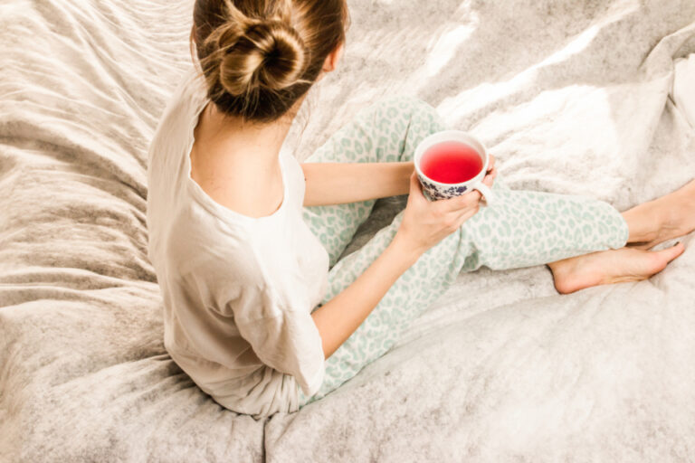 Woman resting on a cozy bed with a cup of tea, a calm self-care moment during the menstrual cycle