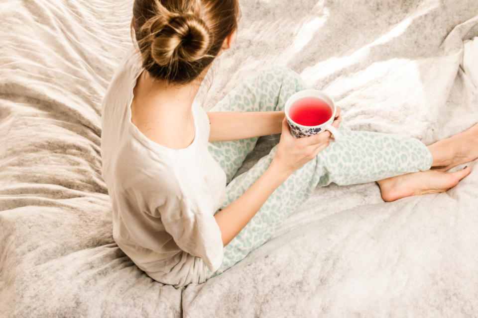 Woman resting on a cozy bed with a cup of tea, a calm self-care moment during the menstrual cycle