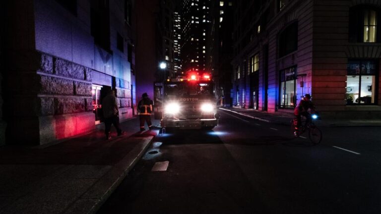 Emergency vehicle with flashing lights on a dark city street at night, a reminder to call 911 in a true emergency