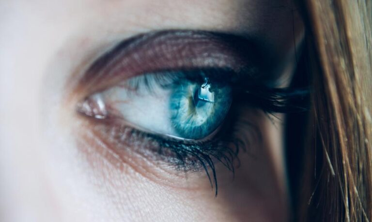 Close-up of a woman's blue-green eye showing the iris and pupil, the parts checked during a dilated eye exam