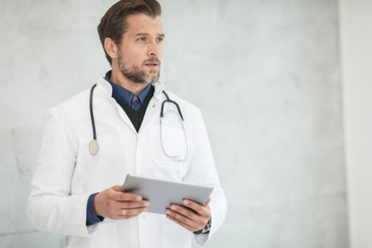 Doctor in a white coat with a stethoscope holding a tablet, ready to review your health at a routine visit