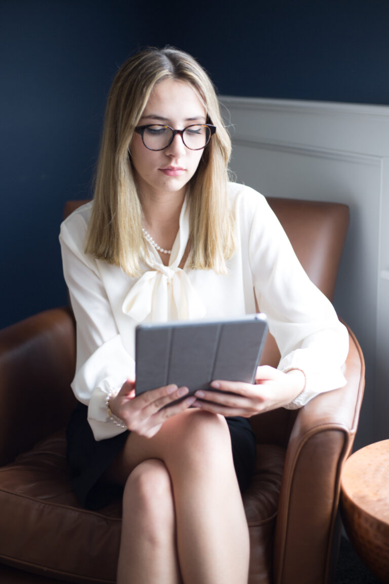 Woman with glasses calmly reading health information on a tablet while sitting in a leather armchair at home